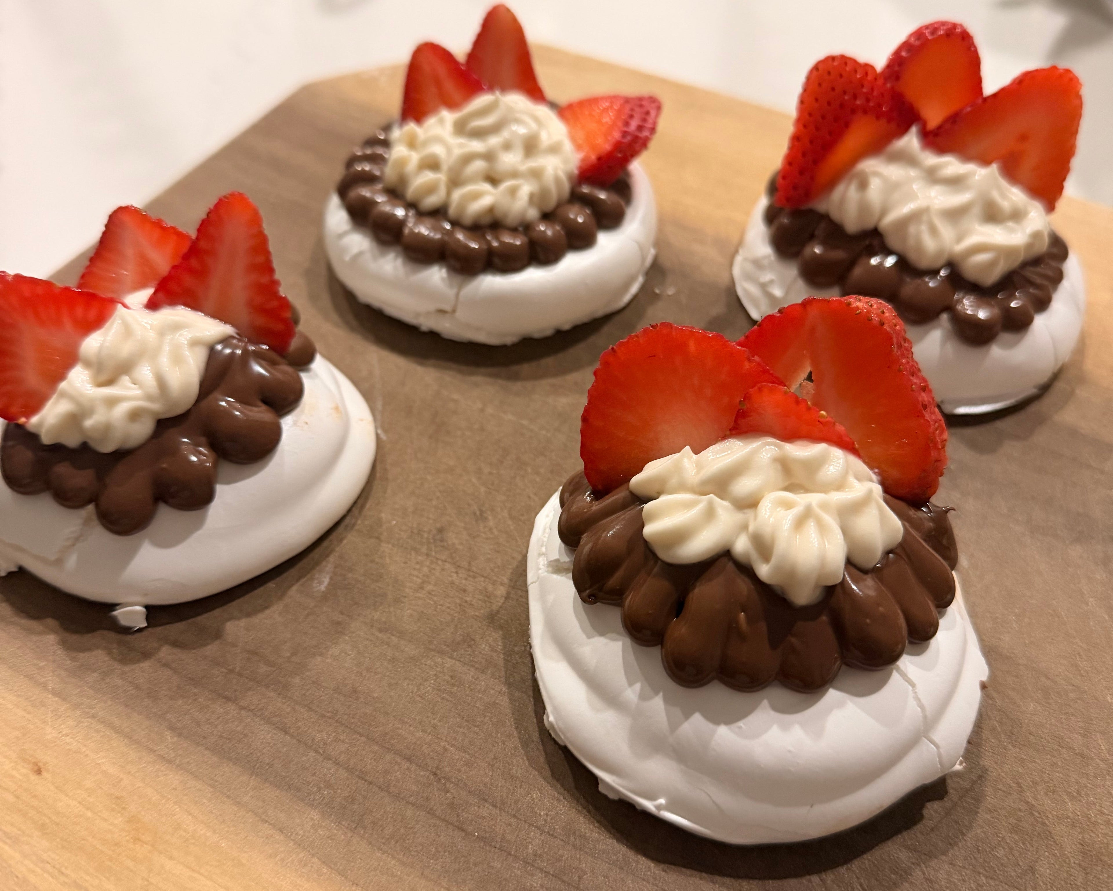 Small dessert plates with strawberry and chocolate toppings on a wooden surface.